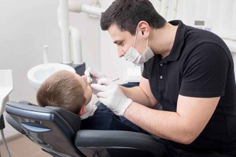 Pediatric dentist examining teeth of boy patient in dental clinic using dental tools